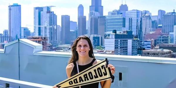 alumni holding Colorado pennant in front of skyline