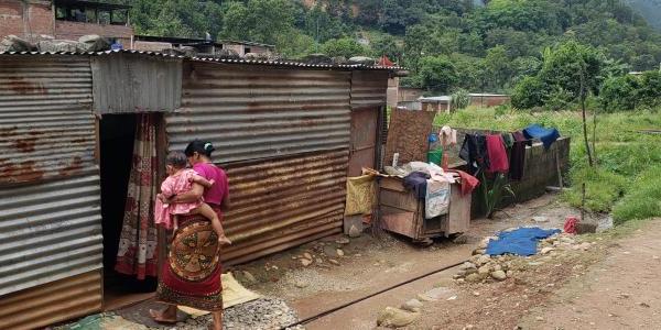 Woman carrying baby walking into corrugated metal home