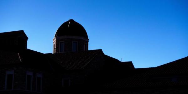 Silhouette of a building on campus in front of a bluebird sky