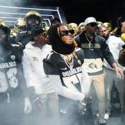 Artist Lil Wayne is surrounded by football players, Coach Prime, Chip and others. A slight mist floats in the air. (Photo by David Marckel/University of Colorado)