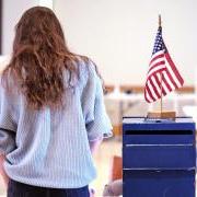 person standing next to a vote dropbox with an American flag