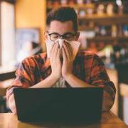 Person covering their face with a tissue while working on a laptop