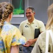 Justin Schwartz, holding a black folio under his right arm smiles as three people look on, forming a circle around him.