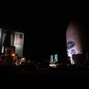 Satellite labeled "GOES" sits next to a large hangar labeled "NASA" at night time