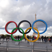 Statue of five Olympic rings in foreground with plaza and Eiffel Tower in the background