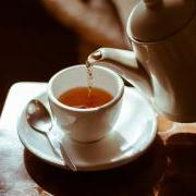 Tea is poured from a white kettle into a white cup. 